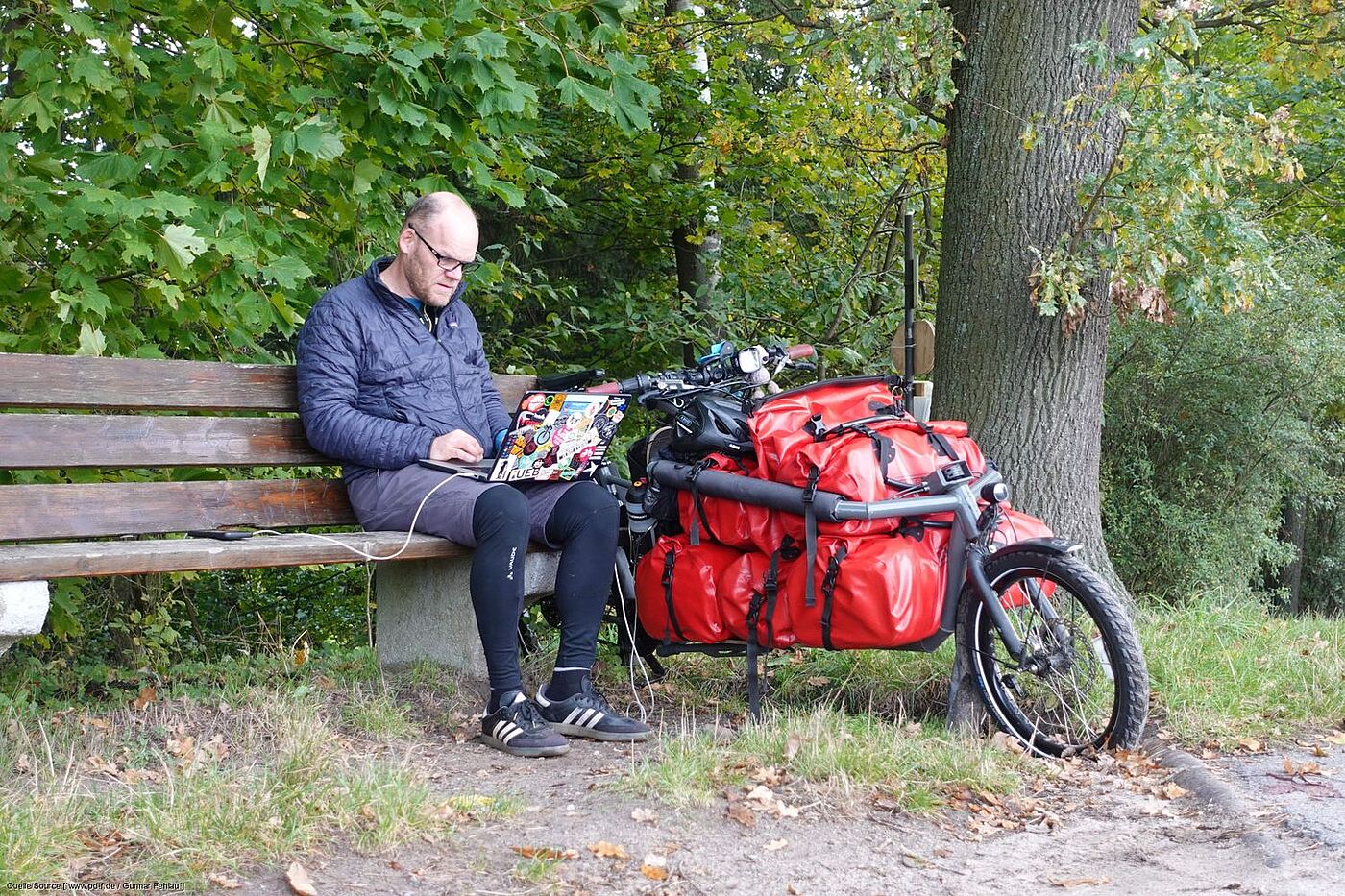 Arbeit auf Parkbank Gunnar Fehlau sitzt auf einer Bank und arbeitet am Laptop. Sein Lastenrad steht neben ihm.