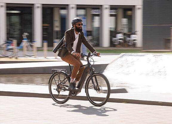Urbane Mobilität: Geschäftsmann auf einem Elektrofahrrad in der Stadt Ein Pendler fährt auf seinem elektrischen Fahrrad durch das Stadtgebiet.