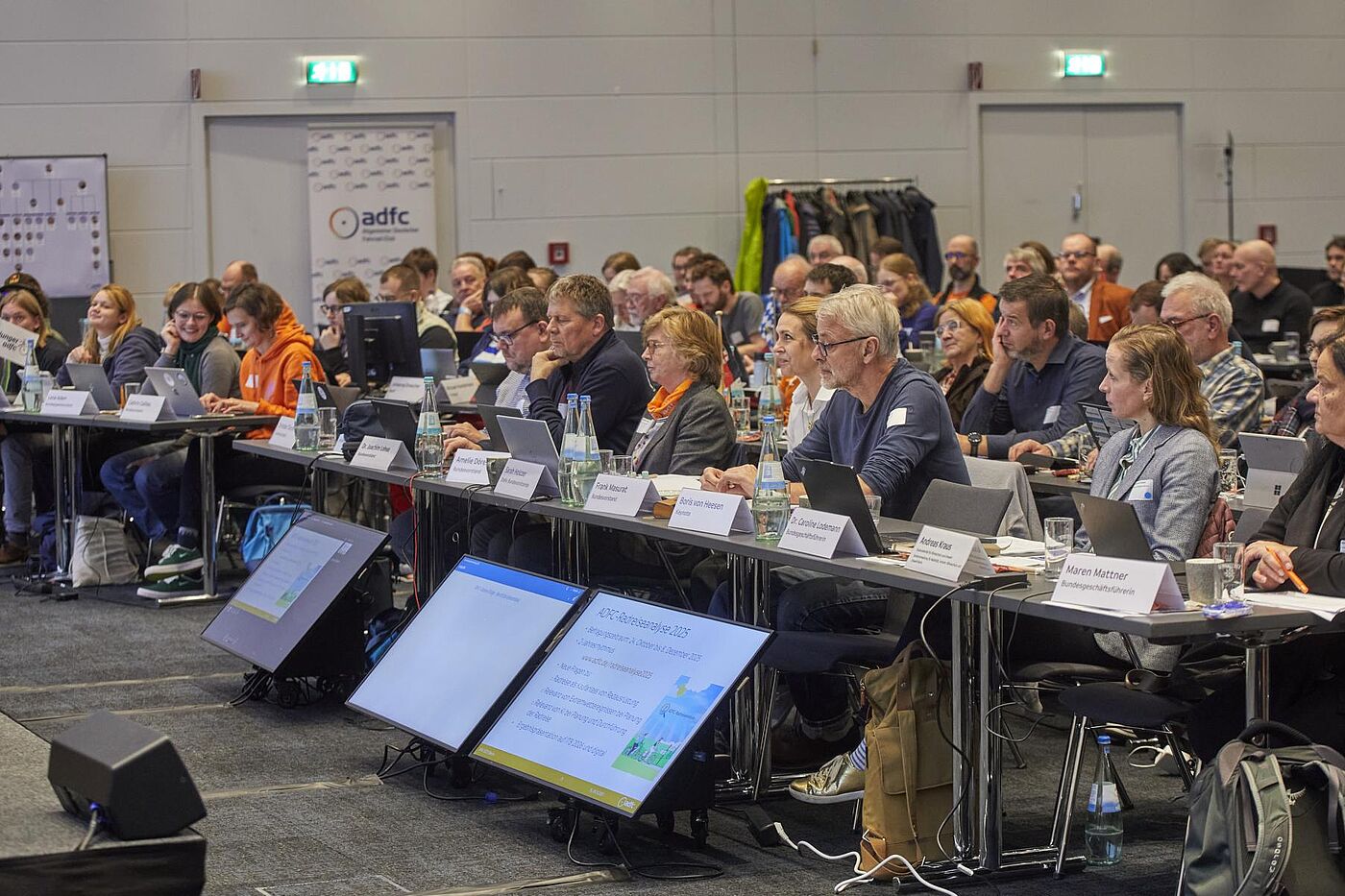 Teilnehmende sitzen in einem großen Konferenzraum an langen Tischen, arbeiten an Laptops und folgen der BHV 2025.
