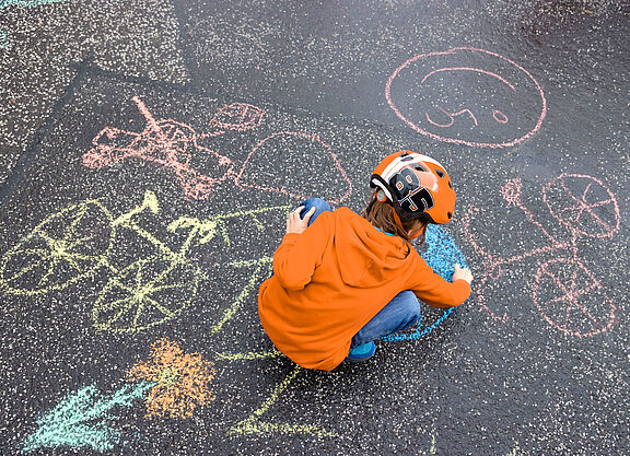 Header Kidical Mass Materialien Ein Kind malt mit Kreide Fahrräder auf die Straße