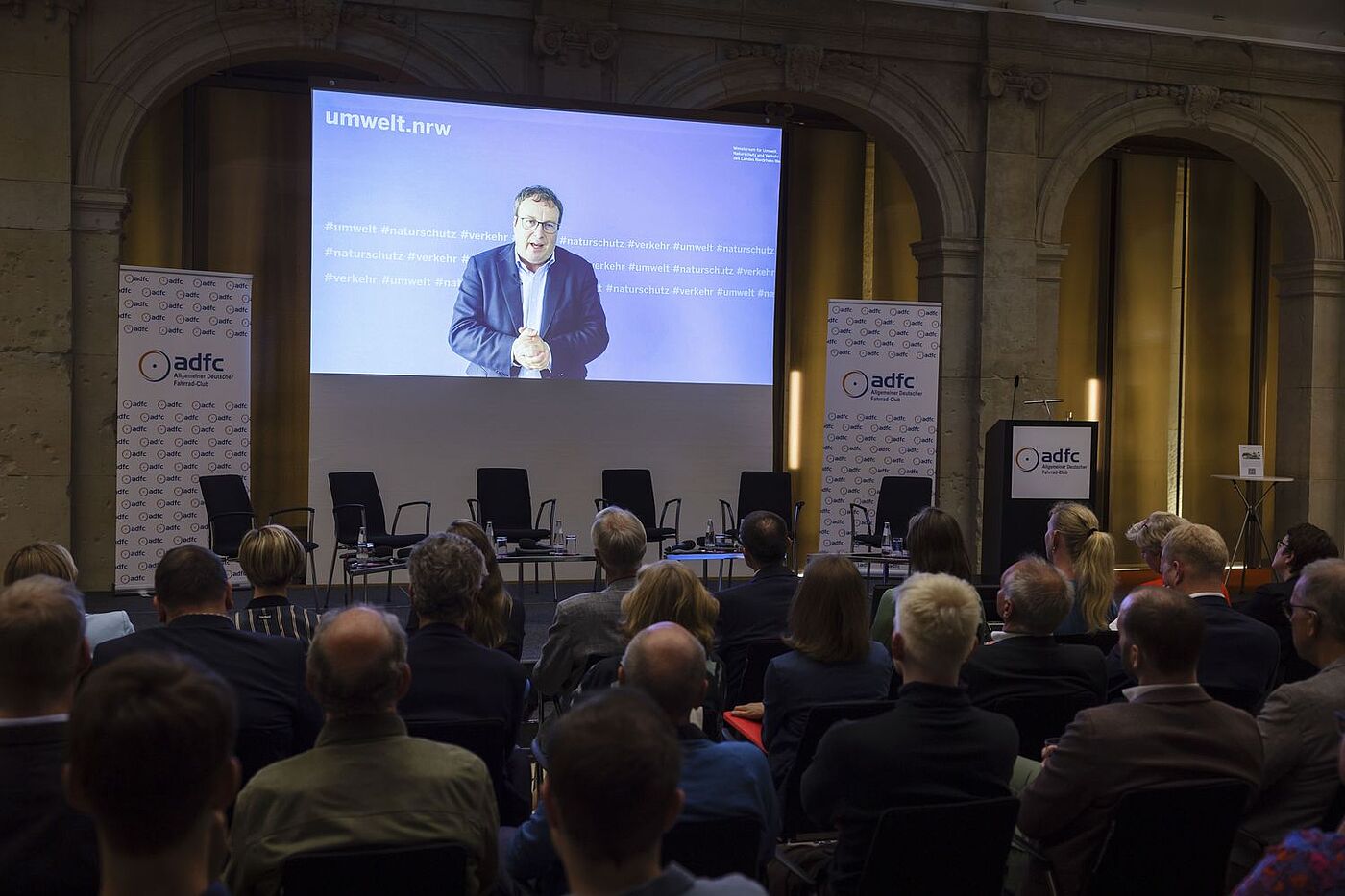 ADFC | Parlamentarischer Abend am 6. Juni 2024 Auf der Videoleinwand ist Oliver Krischer, Minister für Umwelt, Naturschutz und Verkehr des Landes Nordrhein-Westfalen, zu sehen, der ein Grußwort spricht.