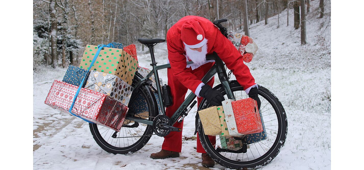 Weihnachtsmann Man in Weihnachtskleidung beugt sich über ein mit Geschenken beladenes Fahrrad im Schnee.